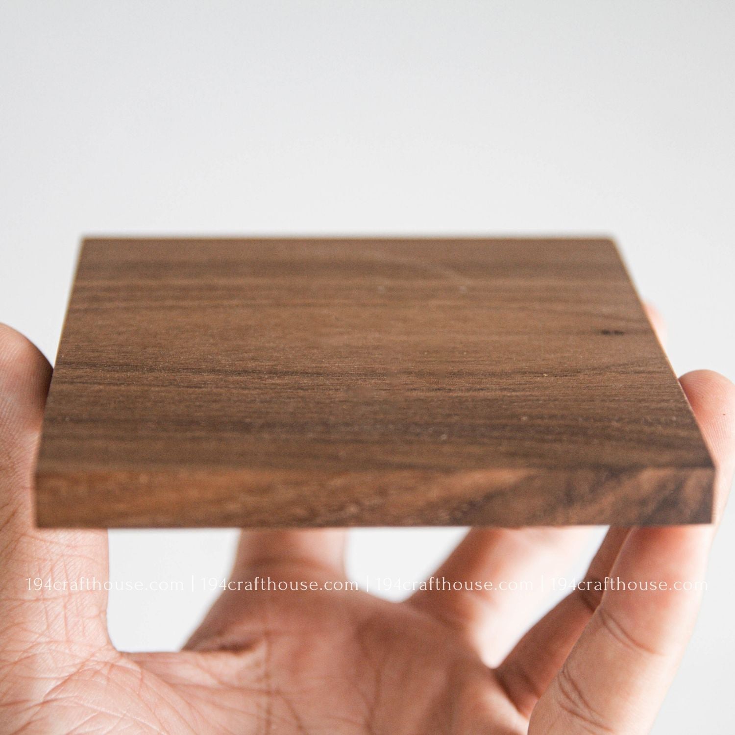 Hand holding a walnut wooden square coaster with a plain background