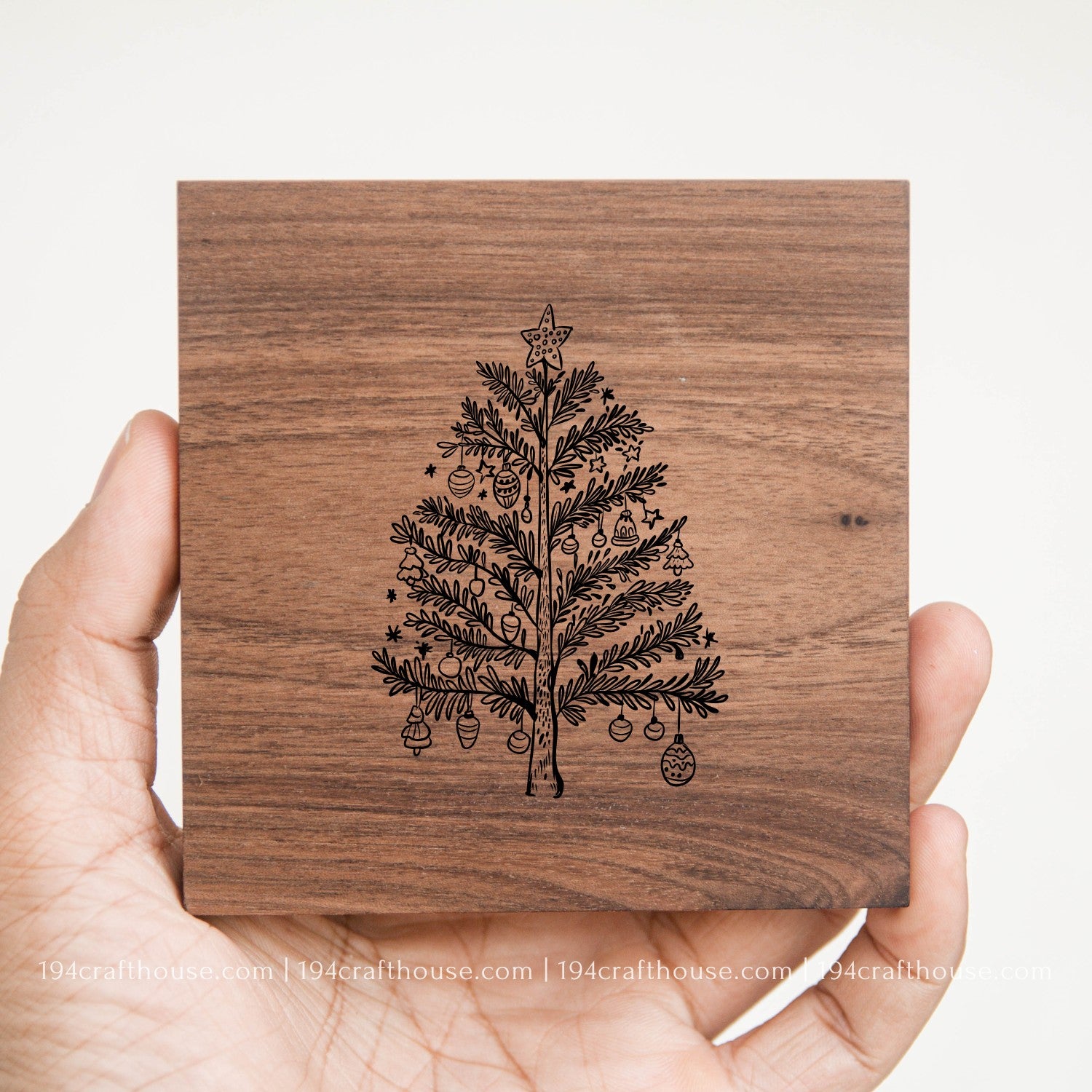 Wooden coaster with a laser-cut Christmas tree design held by a hand on a white background