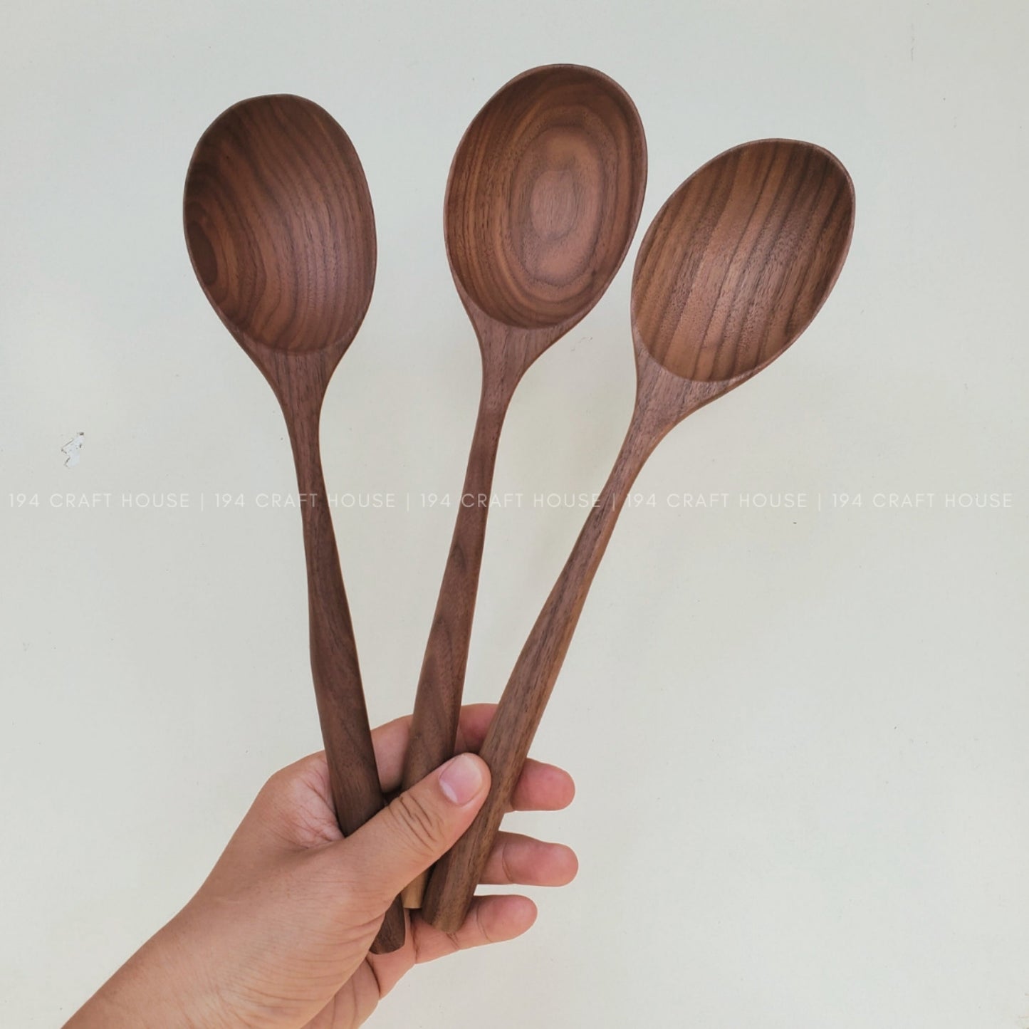 Three walnut wooden spoons held by a hand against a plain background