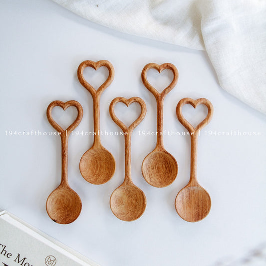 Set of five wooden spoons with heart-shaped handles on a white surface.