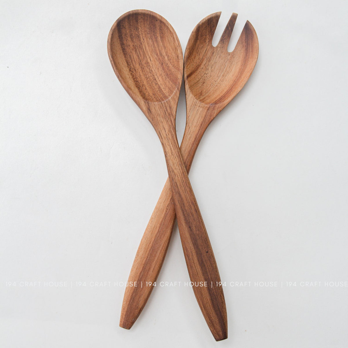 Acacia wood salad spoon and fork in an X shape on a light background, warm brown wood