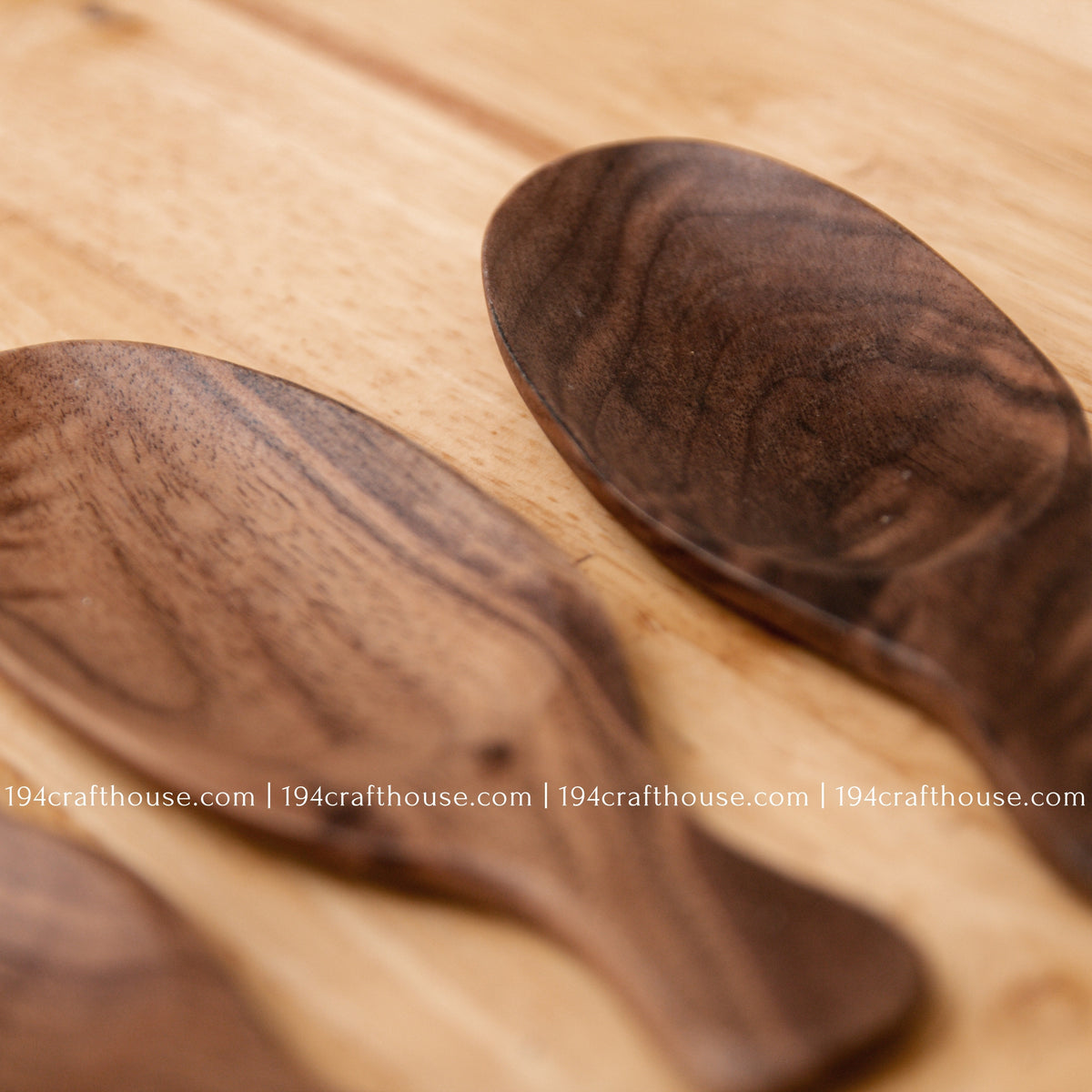 Close-up of a walnut wood tea scoop beside another scoop, highlighting the dark grain and rounded bowl.