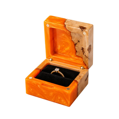 Open square engagement ring box made of orange epoxy resin and natural burl wood, displaying a gold diamond ring on a black velvet lining