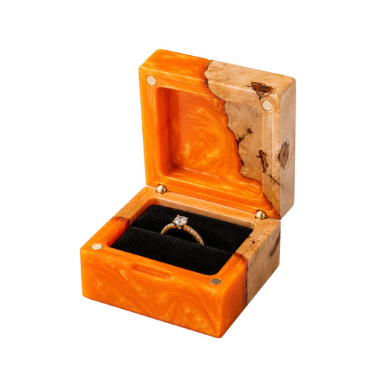 Open square engagement ring box made of orange epoxy resin and natural burl wood, displaying a gold diamond ring on a black velvet lining