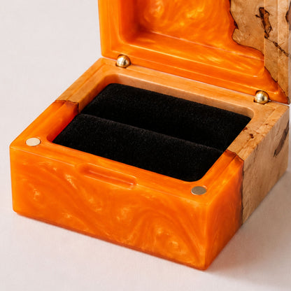 Close-up of an open square ring box made of orange resin and burl wood with a black velvet interior and magnet closure.