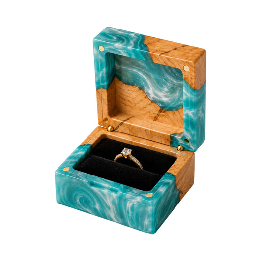 Open square engagement ring box made of turquoise epoxy resin and natural burl wood, displaying a gold diamond ring on a black velvet lining