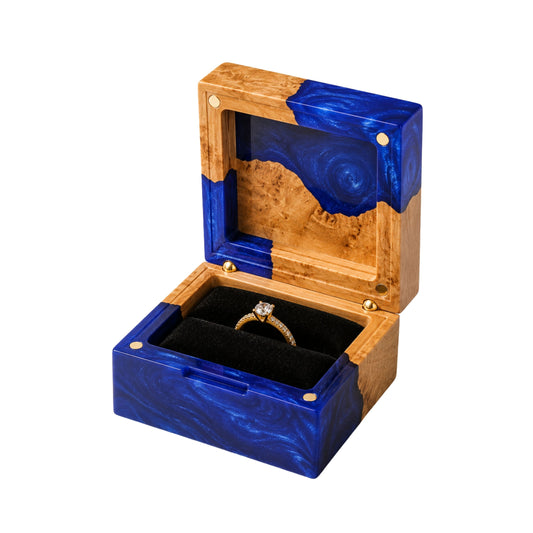 Open square engagement ring box made of blue epoxy resin and natural burl wood, displaying a gold diamond ring on a black velvet lining