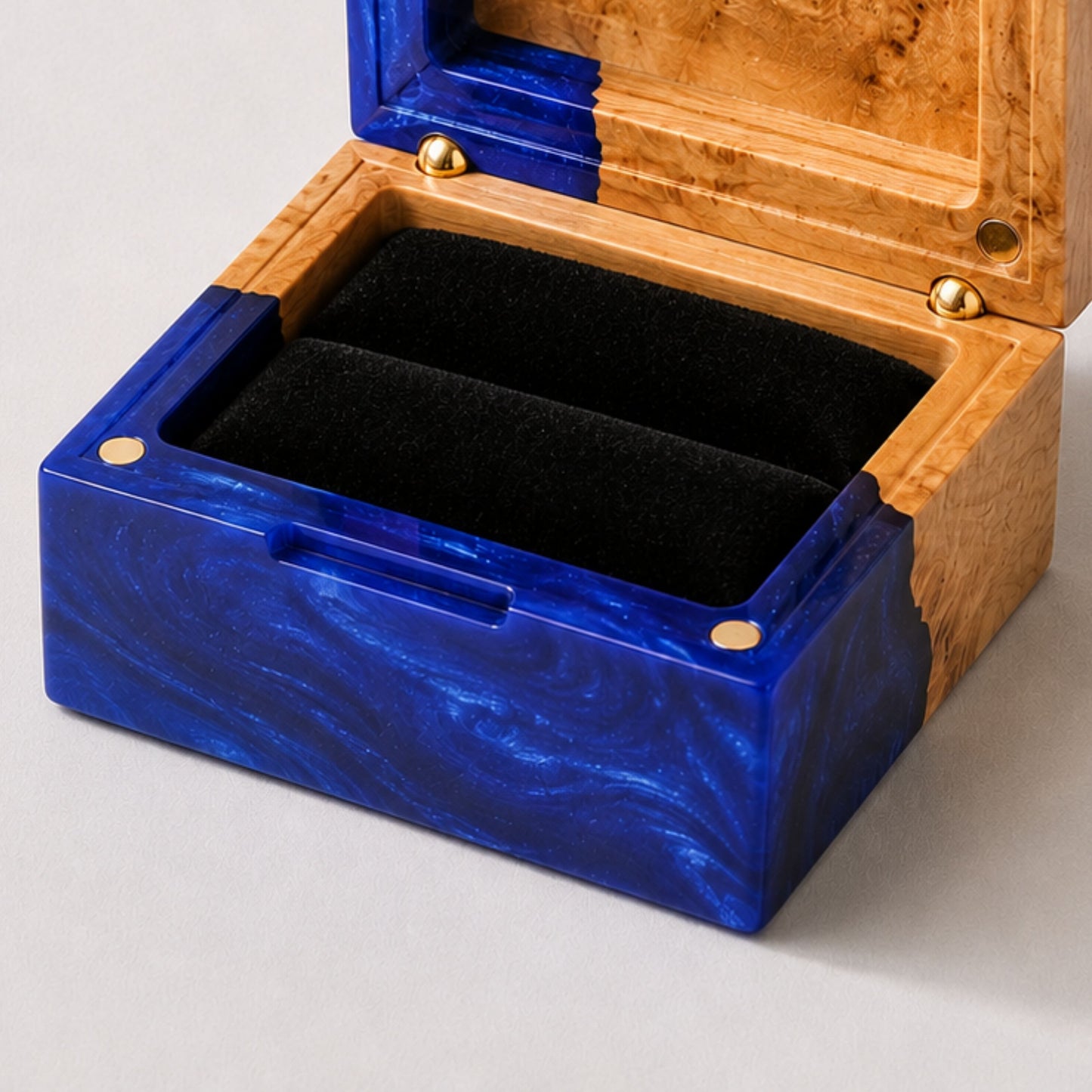 Close-up of an open square ring box made of blue resin and burl wood with a black velvet interior and magnet closure.