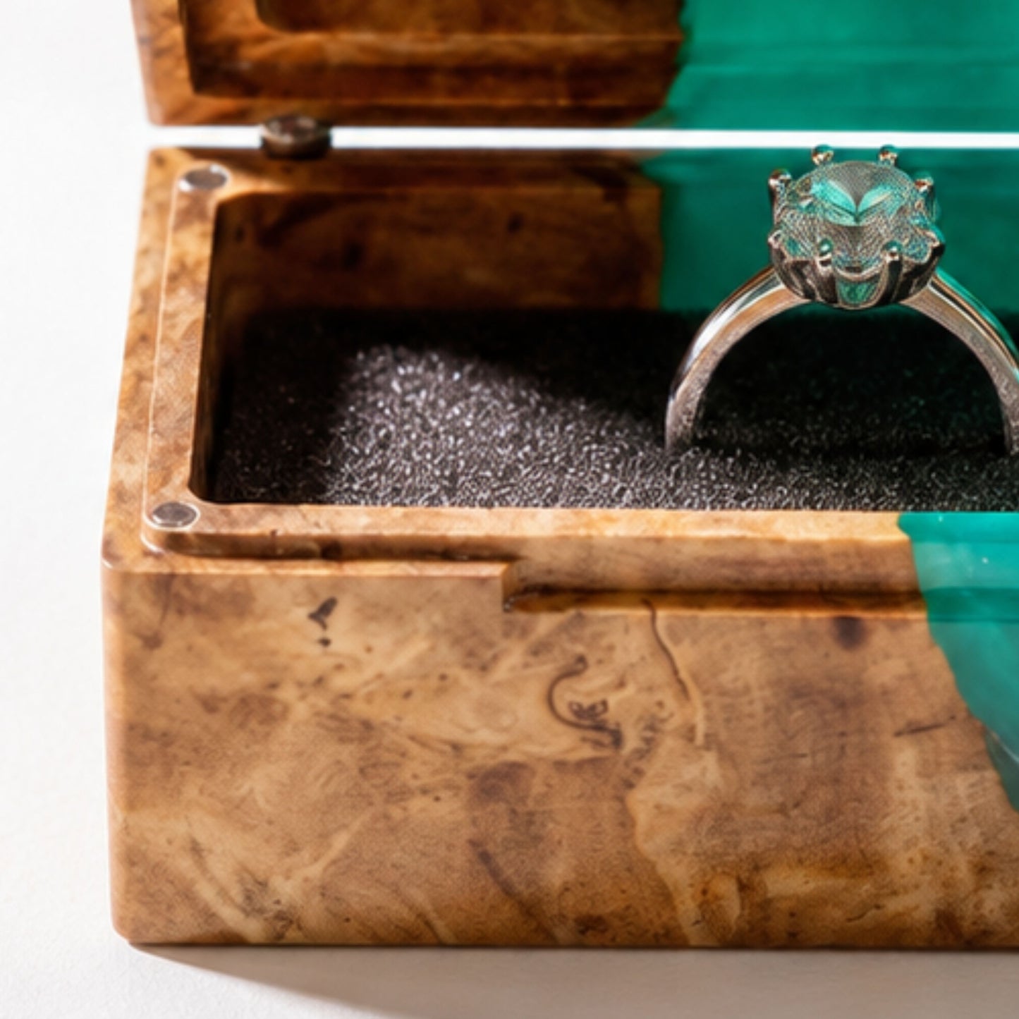 Close-up shot of an engagement ring cushioned inside an open burl wood and turquoise epoxy resin ring box.