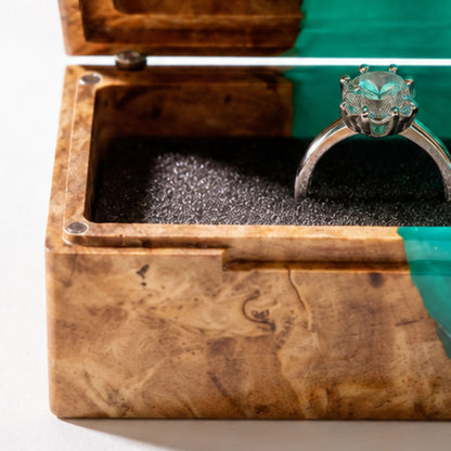 Close-up shot of an engagement ring cushioned inside an open burl wood and turquoise epoxy resin ring box.