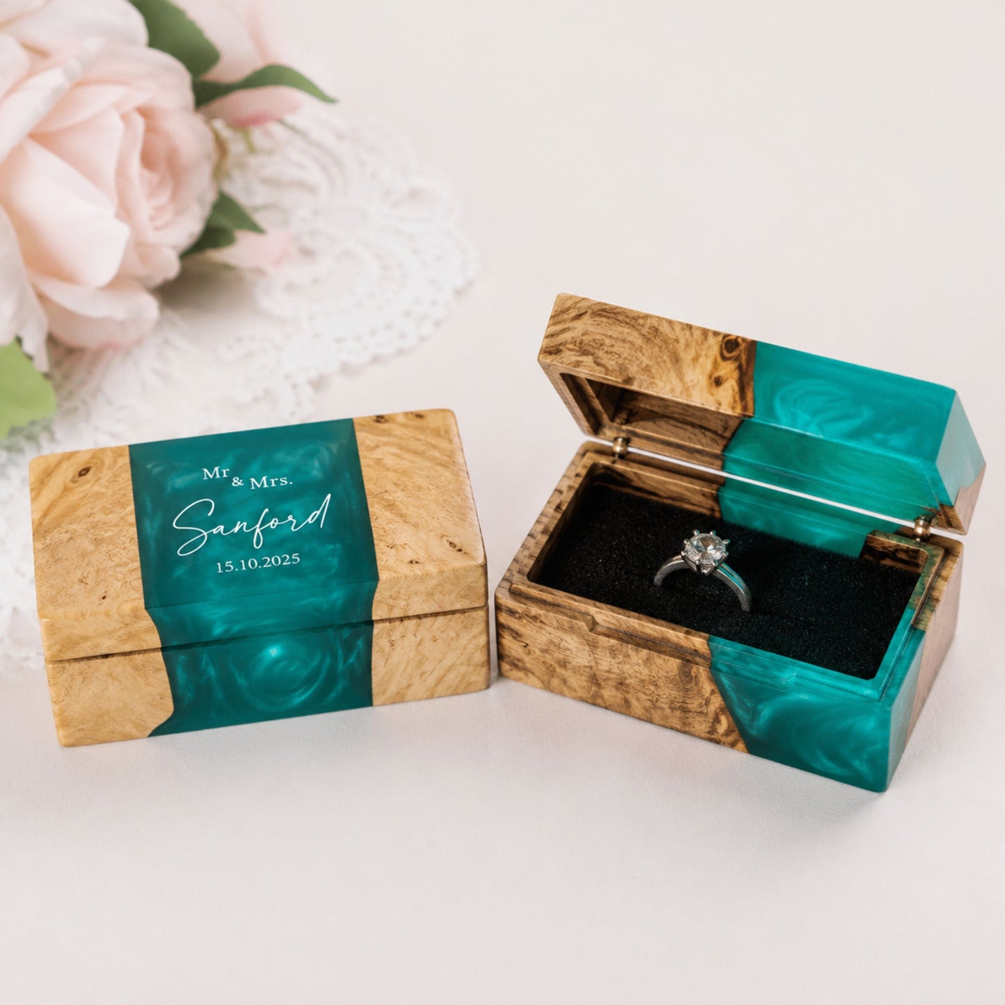Pair of custom engraved wood and turquoise resin ring boxes set on a wedding styled table alongside pink roses.
