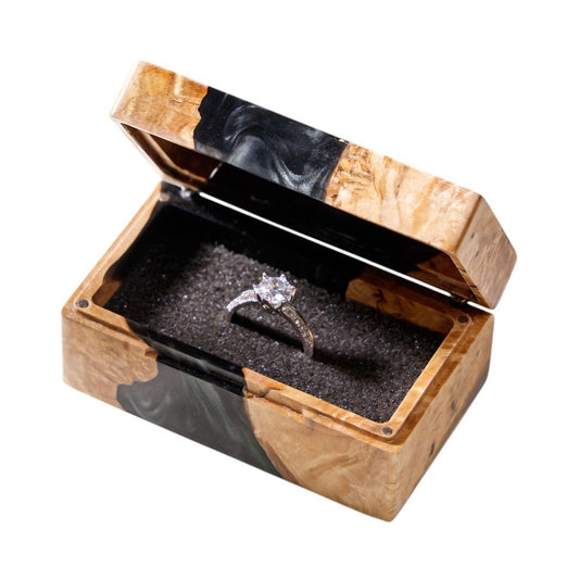 Open handcrafted wood and black epoxy resin engagement ring box displaying a proposal diamond ring inside a black velvet slot.
