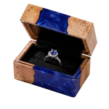 Open handcrafted wood and blue epoxy resin engagement ring box displaying a proposal diamond ring inside a blue velvet slot.

