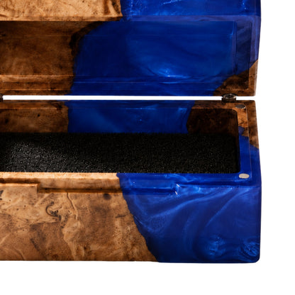 Close-up shot of an engagement ring cushioned inside an open burl wood and blue epoxy resin ring box.
