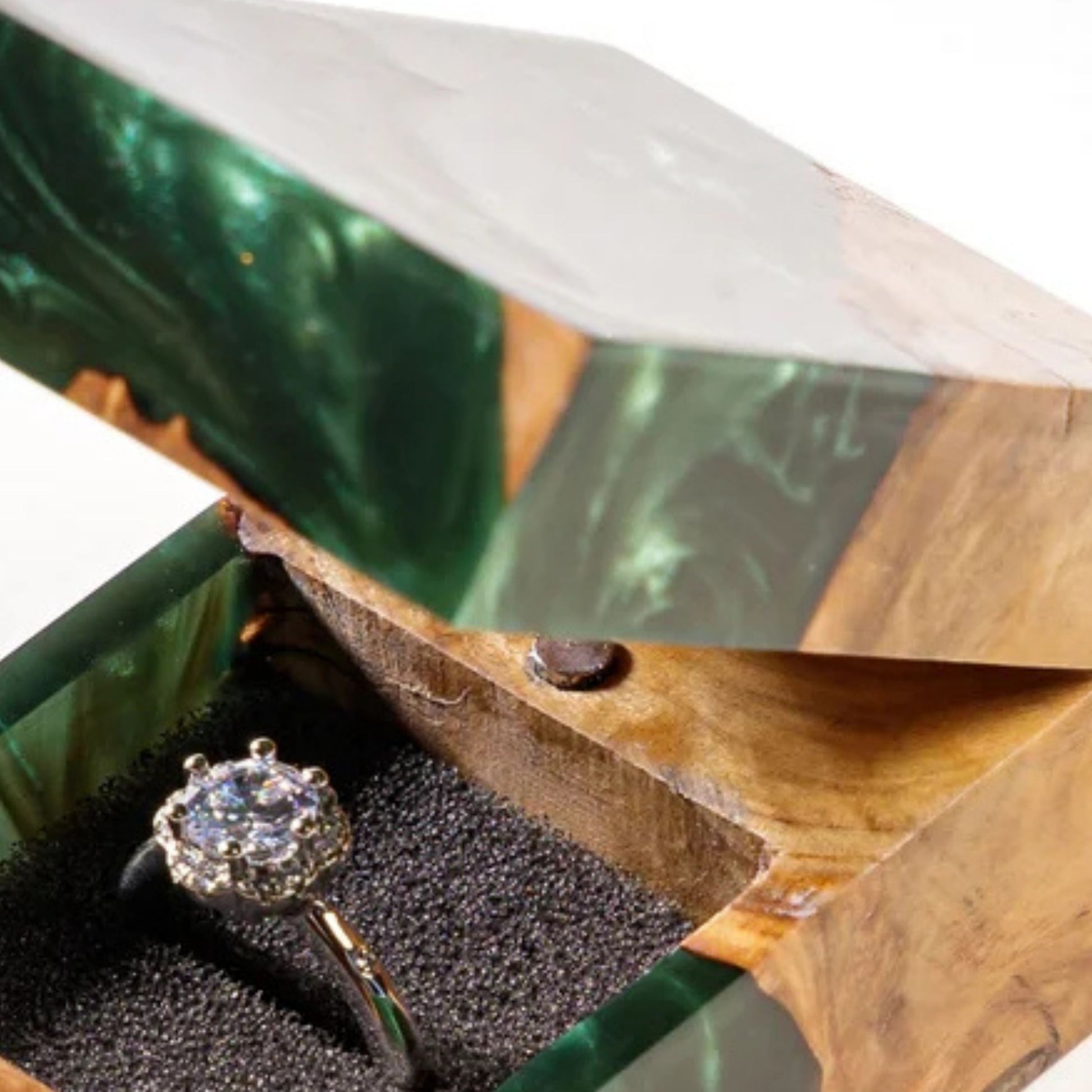 Close-up view of the interior magnetic latch and padded ring insert of an open green resin ring box with a diamond ring.