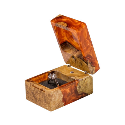 Open orange epoxy resin and natural burl wood ring box holding a diamond engagement ring in a black interior slot.