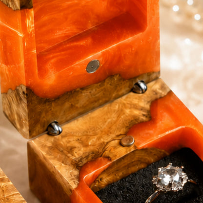 Close-up view of the interior magnetic hinges and velvet ring slot of an open orange resin ring box with a solitaire ring.