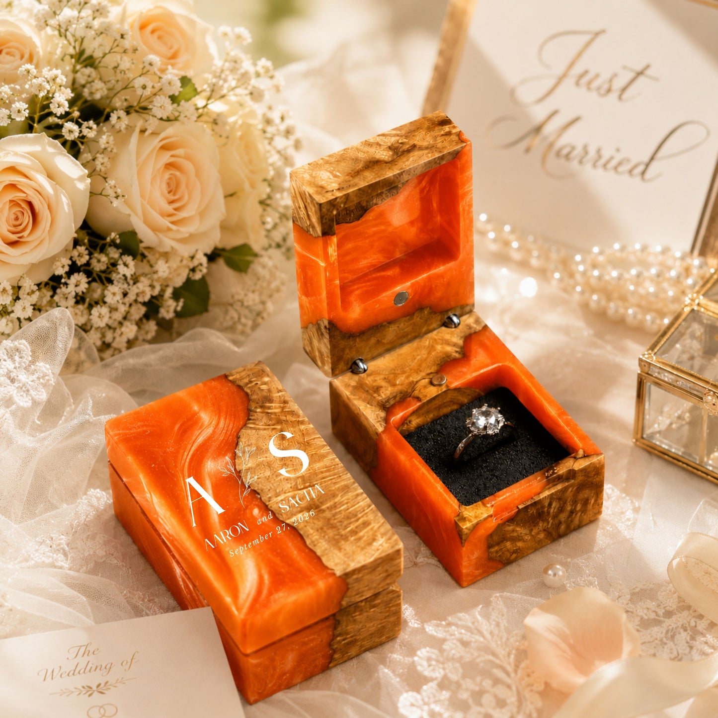 Personalized orange resin and wood ring box engraved with initials and date set in a wedding scene with flowers and candles.