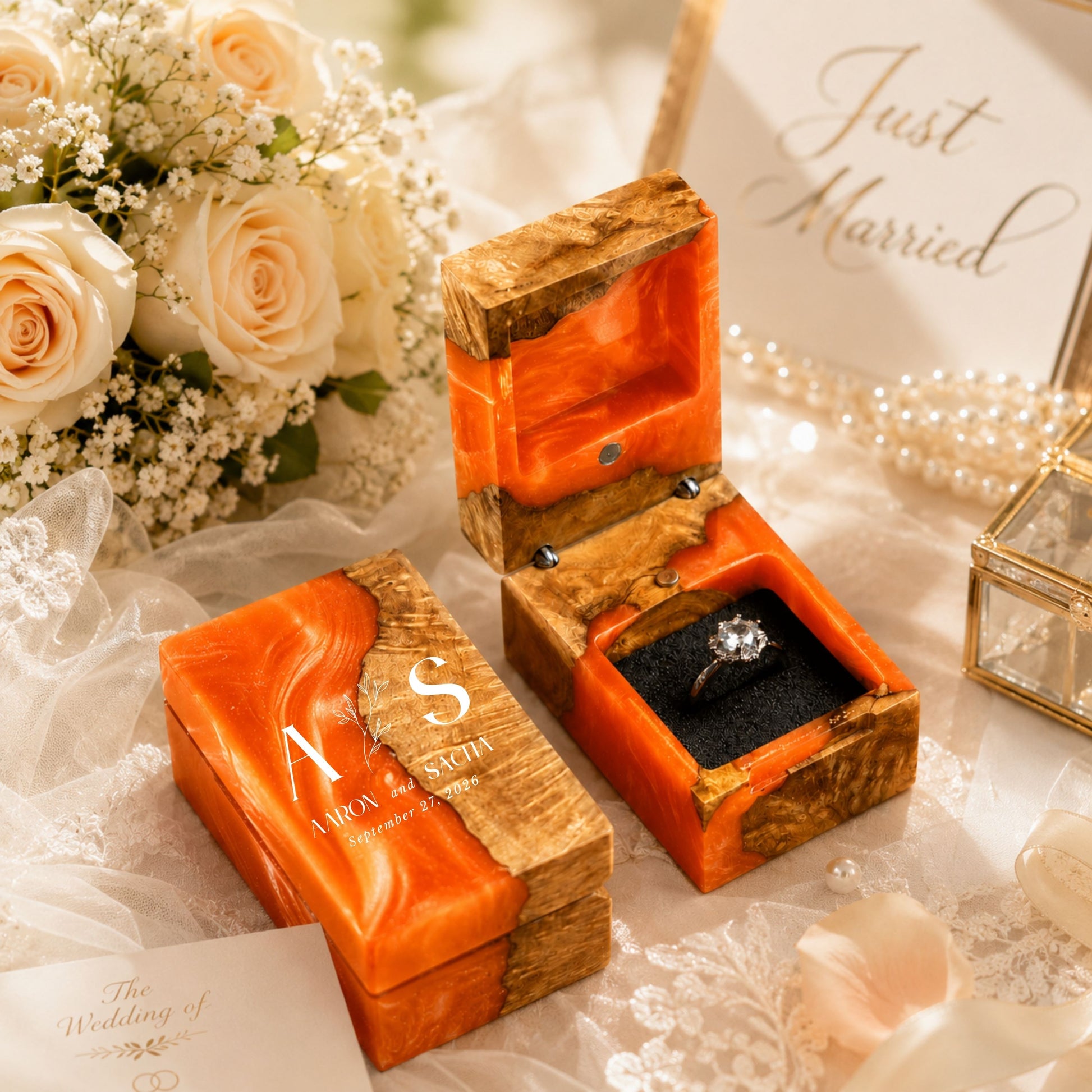 Personalized orange resin and wood ring box engraved with initials and date set in a wedding scene with flowers and candles.