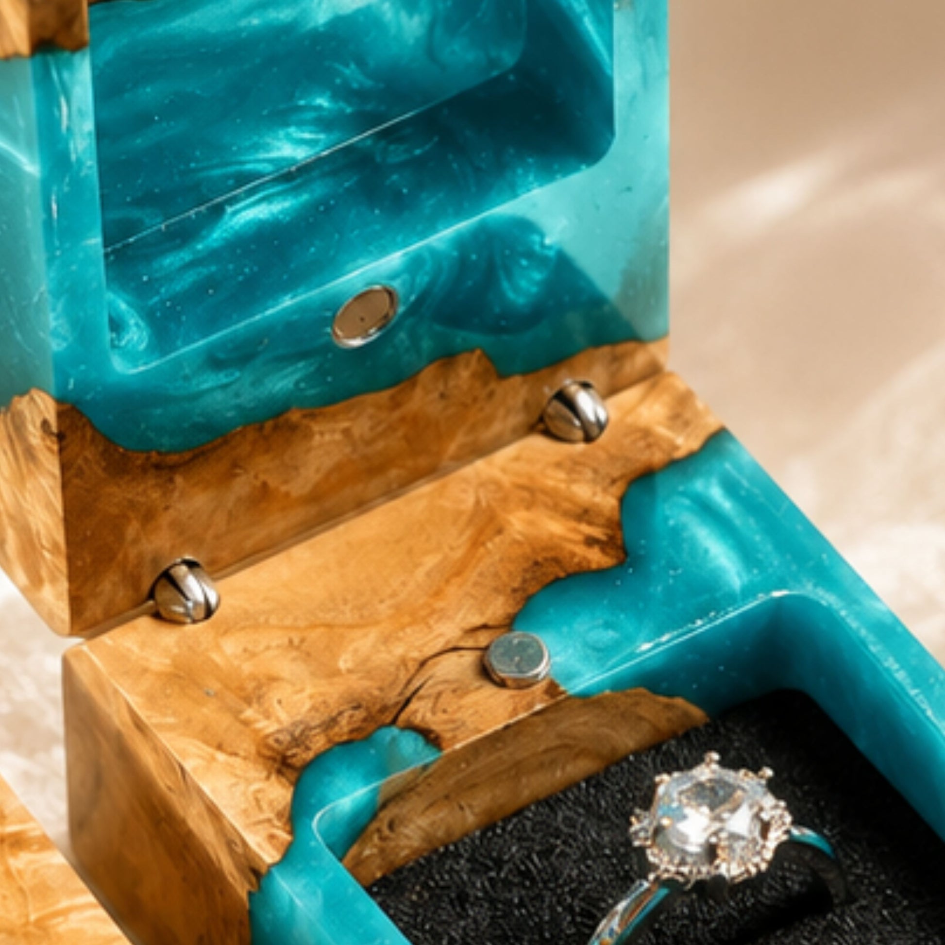 Close-up view of the interior magnetic hinges and velvet ring slot of an open turquoise resin ring box with a diamond ring.