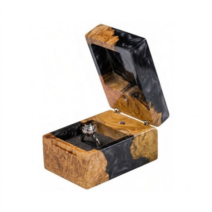 Open black epoxy resin and natural burl wood ring box holding a solitaire diamond engagement ring in a black interior slot.