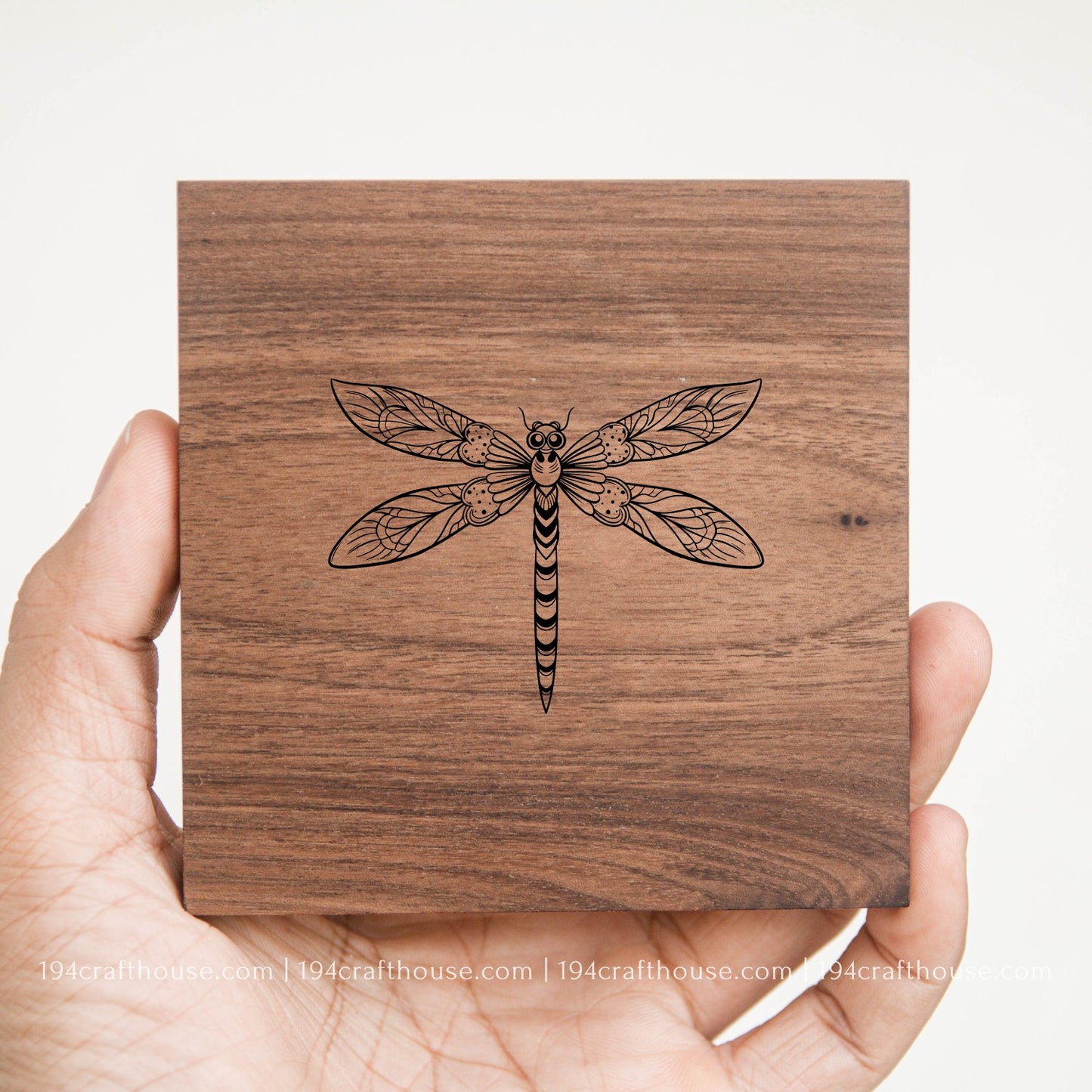 Wooden coaster with laser-cut dragonfly design held by a hand on a white background