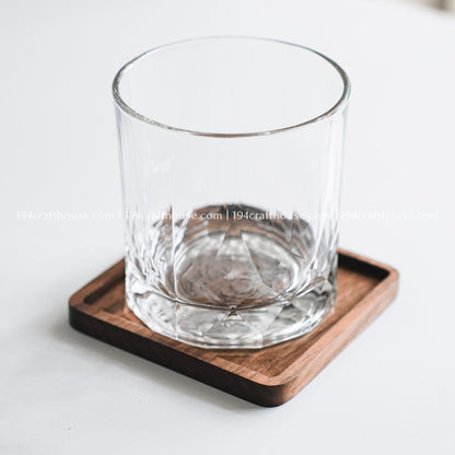 Drinking glass placed on a personalized square walnut wood coaster with handcrafted details