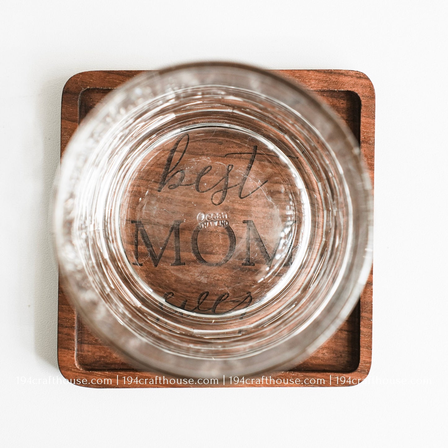 Top-down view of a glass stand on a Best Mom Ever engraved on a single square hand-carved walnut wood coaster with smooth rounded corners on a clean white surface by 194 Craft House