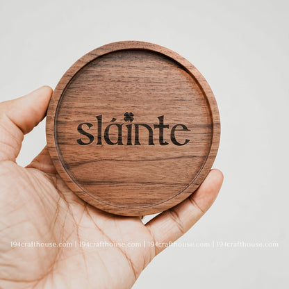 A single round hand-carved walnut wood coaster on hand with engraving text Slainte by 194 Craft House