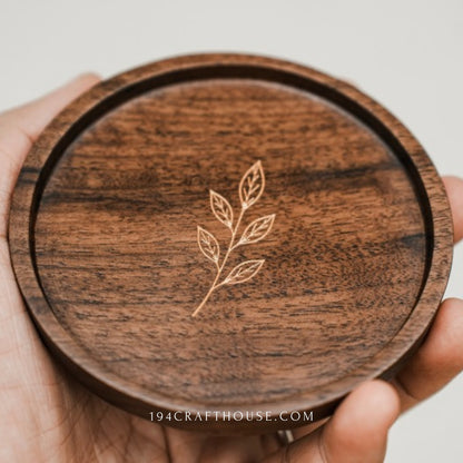 Close view of the engraved leaf sprig on a round walnut coaster held in hands