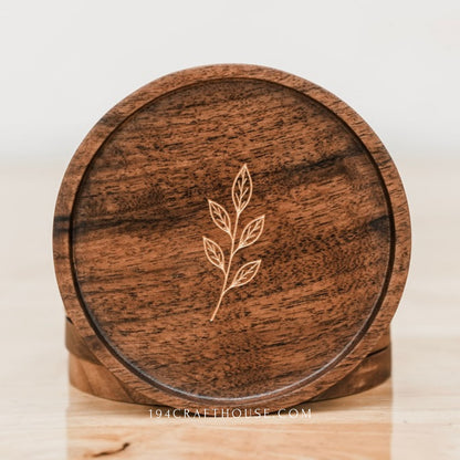 Round walnut coaster with leaf sprig engraving displayed upright with another coaster behind it