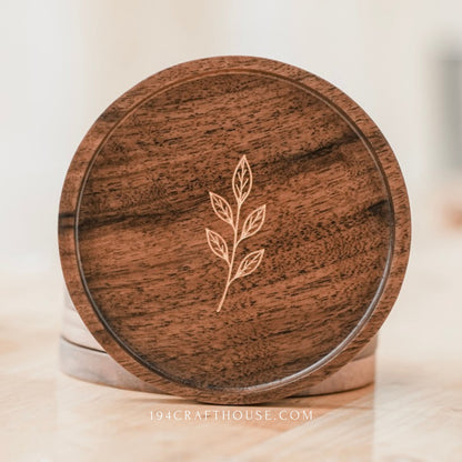 Round walnut coaster with engraved leaf sprig shown upright in a softly lit tabletop display