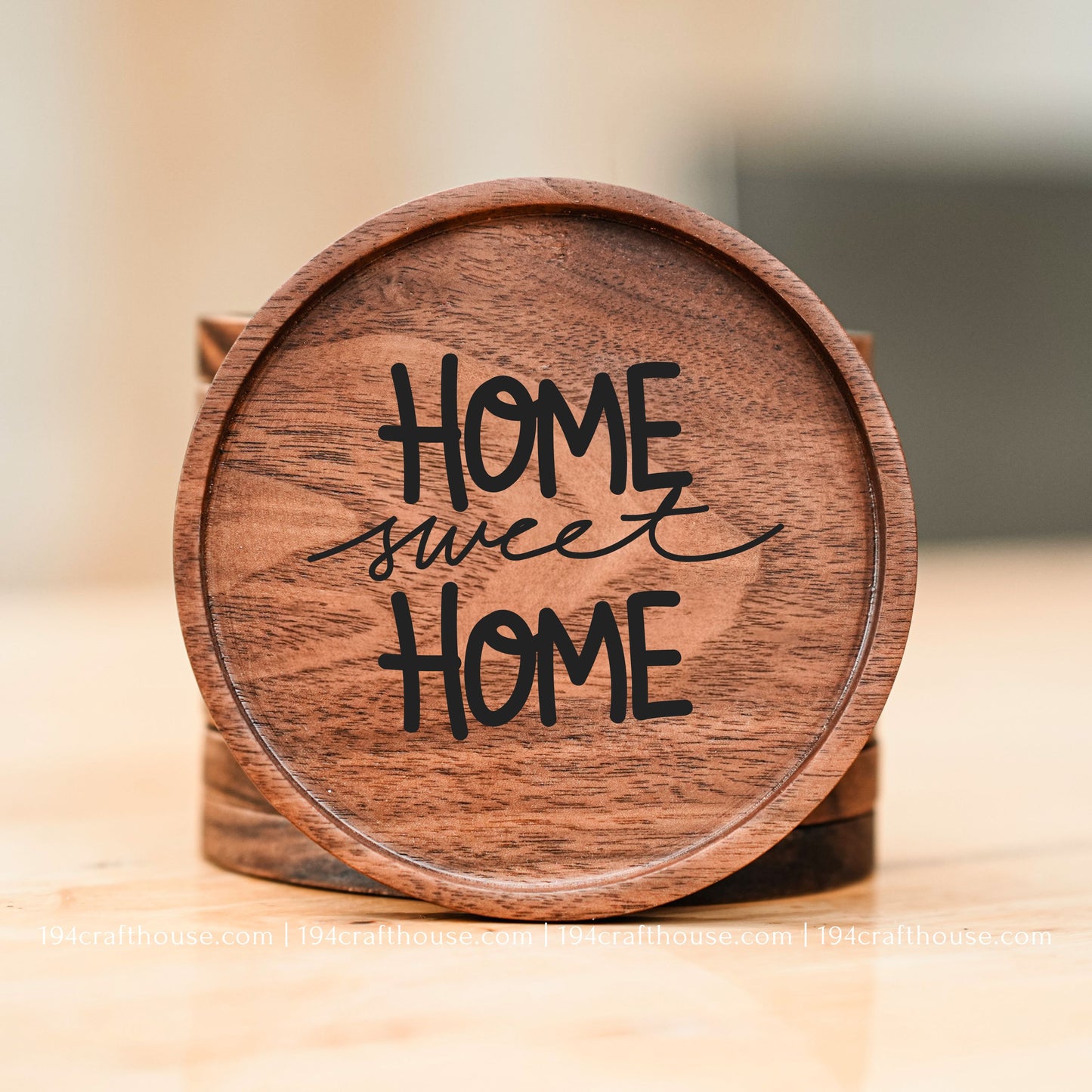A round wooden coastertop with the phrase 'HOME sweet HOME' in black lettering, displayed on a light wooden surface with a softly blurred background.