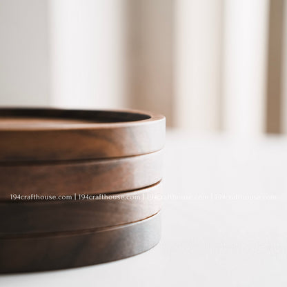 Stacked set of four round walnut wood coasters with a smooth recessed center and natural dark wood grain