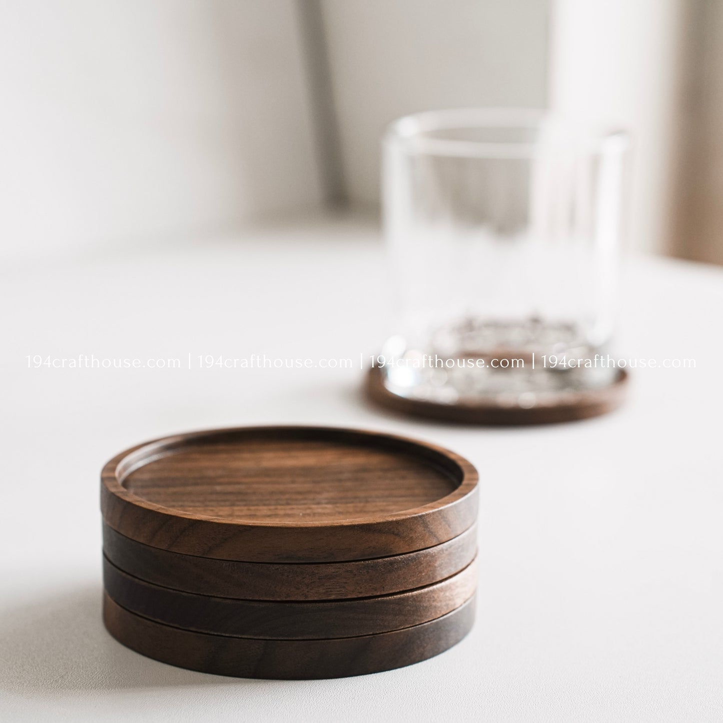 Handcrafted set of 4 round walnut wood coasters displayed with a drinking glass on a clean white background