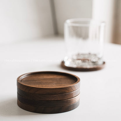 Handcrafted set of 4 round walnut wood coasters displayed with a drinking glass on a clean white background