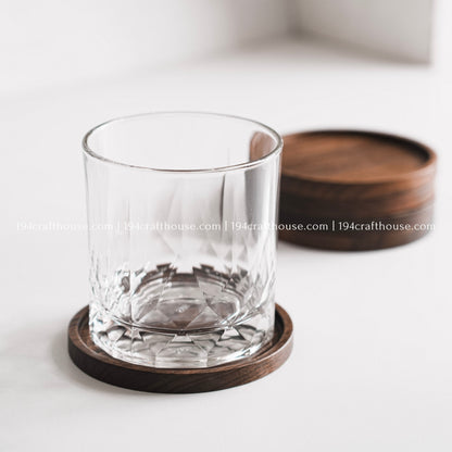 Drinking glass placed on a single handcrafted round walnut wood coaster with natural wood grain