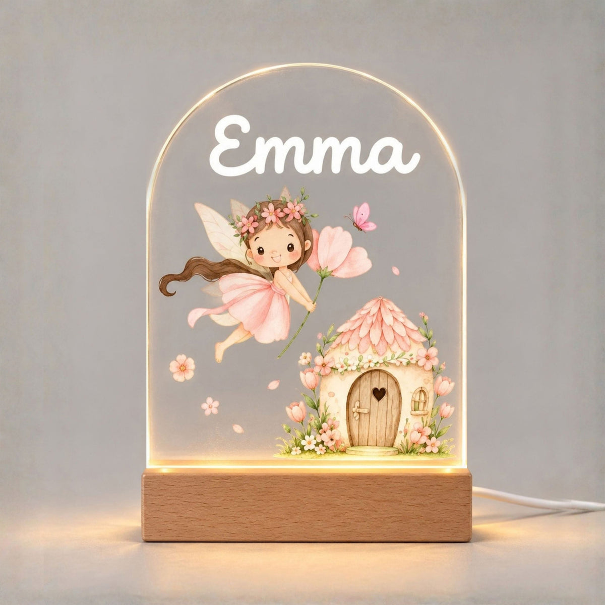 Front view of the illuminated arched night light with fairy and cottage artwork against a pale background.
