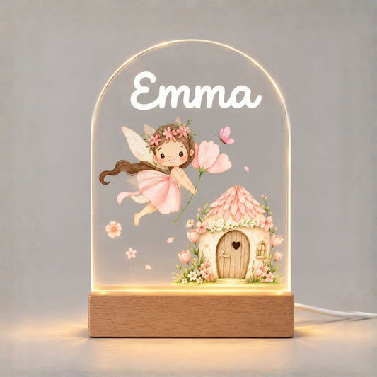 Front view of the illuminated arched night light with fairy and cottage artwork against a pale background.