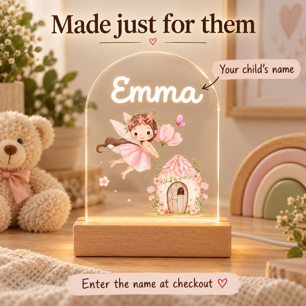 Promotional image points to the name Emma on the fairy cottage night light with a nursery scene behind it.