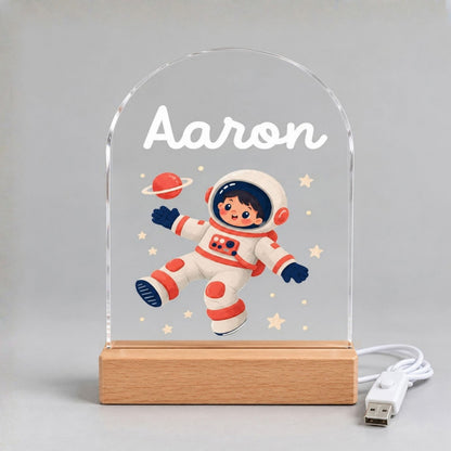 Unlit arched acrylic panel displays the name Aaron, a cartoon astronaut, stars, a planet, wooden base, and USB cable.