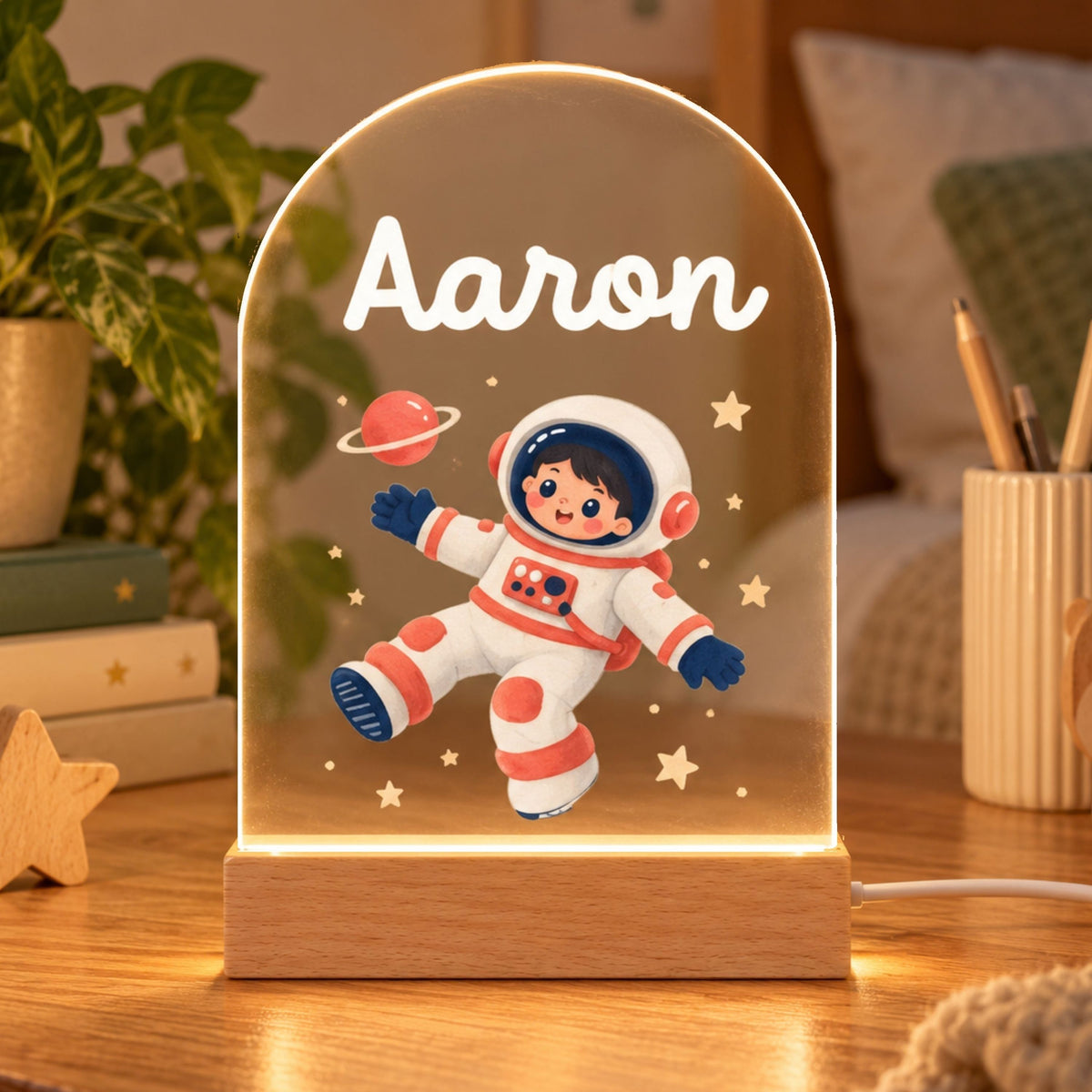 Arched acrylic night light shows Aaron, a cartoon astronaut, stars, and a ringed planet on a wooden base.