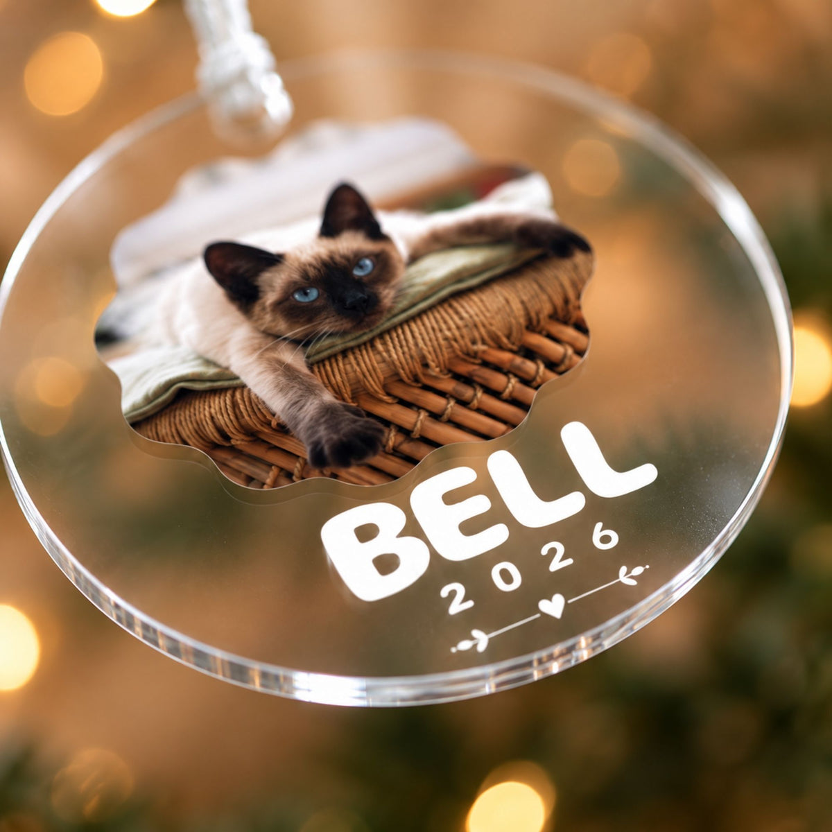 Close-up angled view of a personalized clear acrylic cat ornament showcasing smooth laser-cut edges and white custom text against holiday bokeh lights.