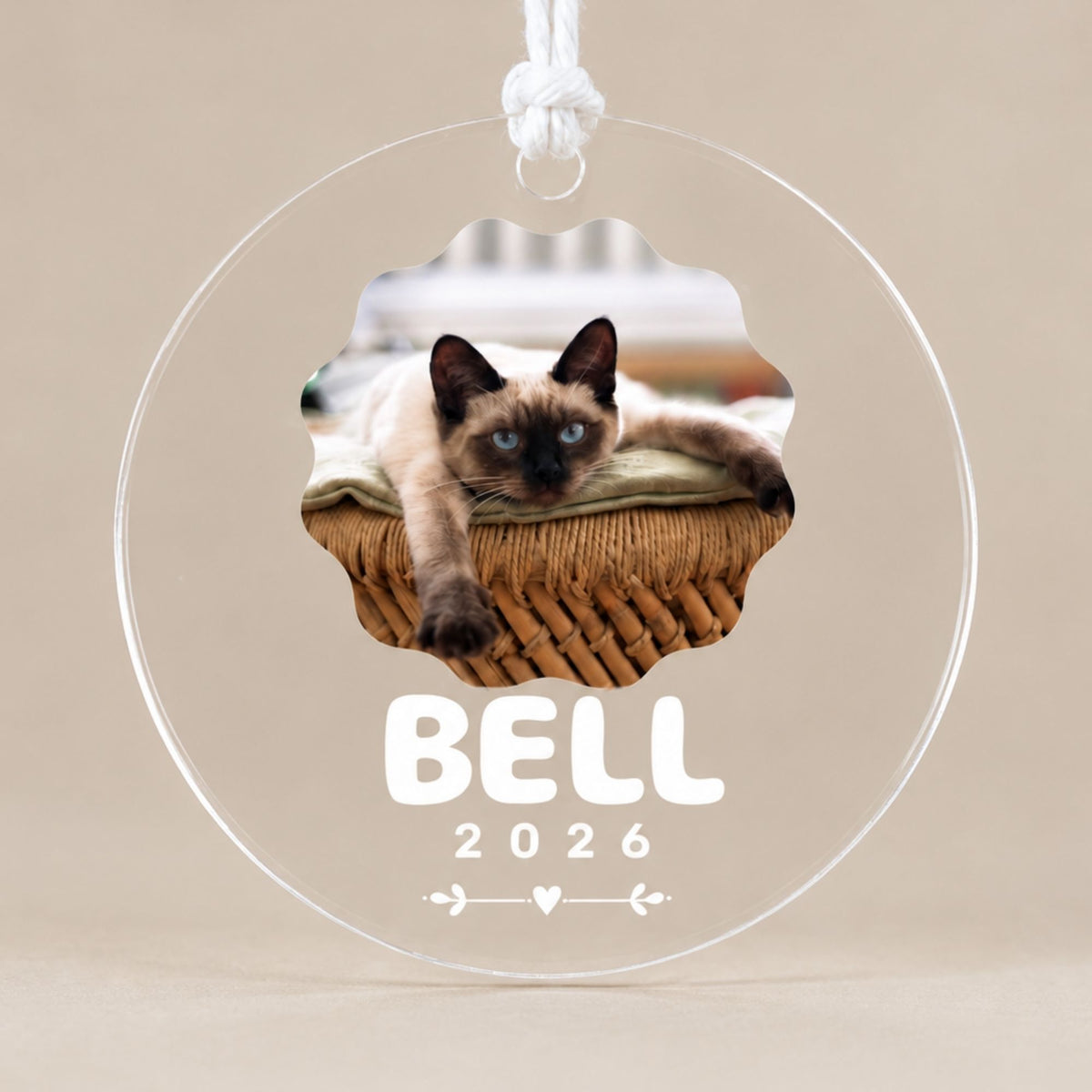 Studio front view of a round clear acrylic pet keepsake ornament printed with a scalloped cat photo, custom name, and year against a neutral beige backdrop.