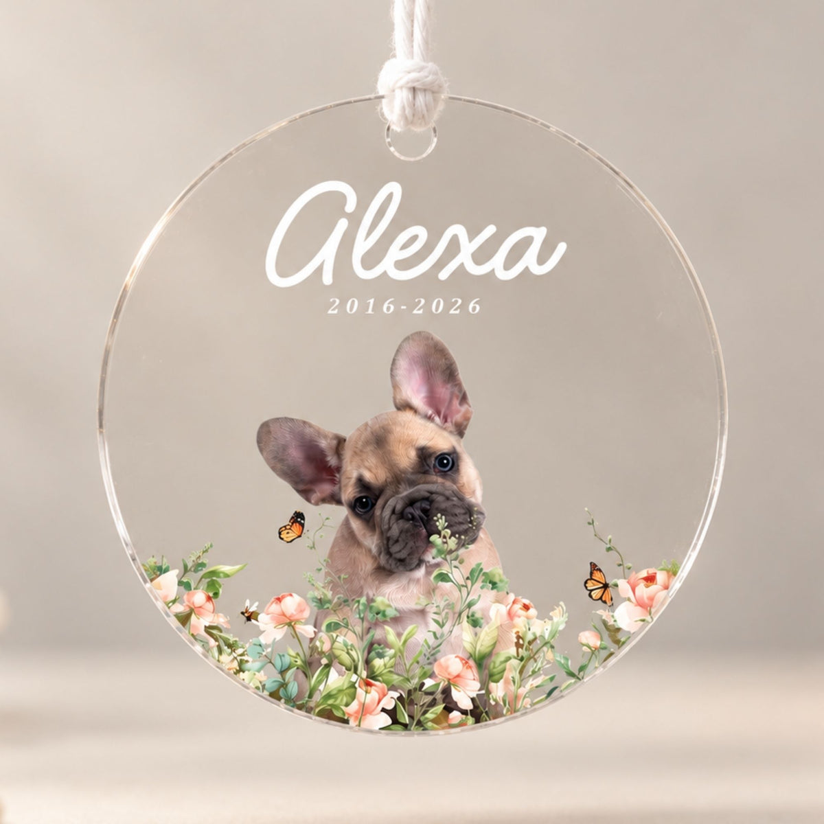 Studio front view of a round acrylic pet loss ornament printed with a French bulldog portrait, floral accents, and custom memorial dates on a neutral background.