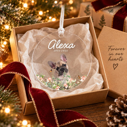 Personalized dog memorial acrylic ornament presented in shredded tissue paper inside a kraft gift box with red velvet ribbon beside a Christmas tree.