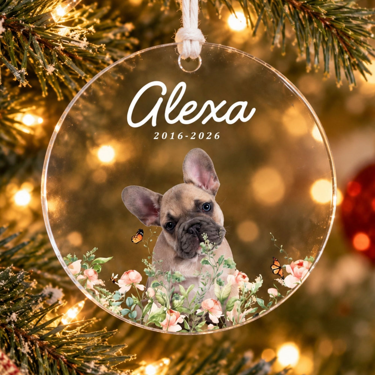 Custom clear acrylic pet memorial ornament featuring a French bulldog puppy in watercolor flowers, name Alexa, and years 2016-2026 on a lit Christmas tree.