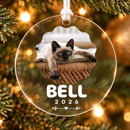Custom clear acrylic Christmas ornament featuring a personalized Siamese cat photo, name Bell, and year 2026 hanging on an illuminated Christmas tree.