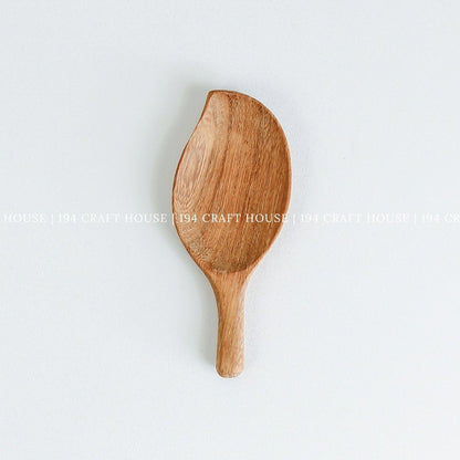 Handcrafted leaf-shaped wooden measuring scoop with smooth natural wood grain on a white background
