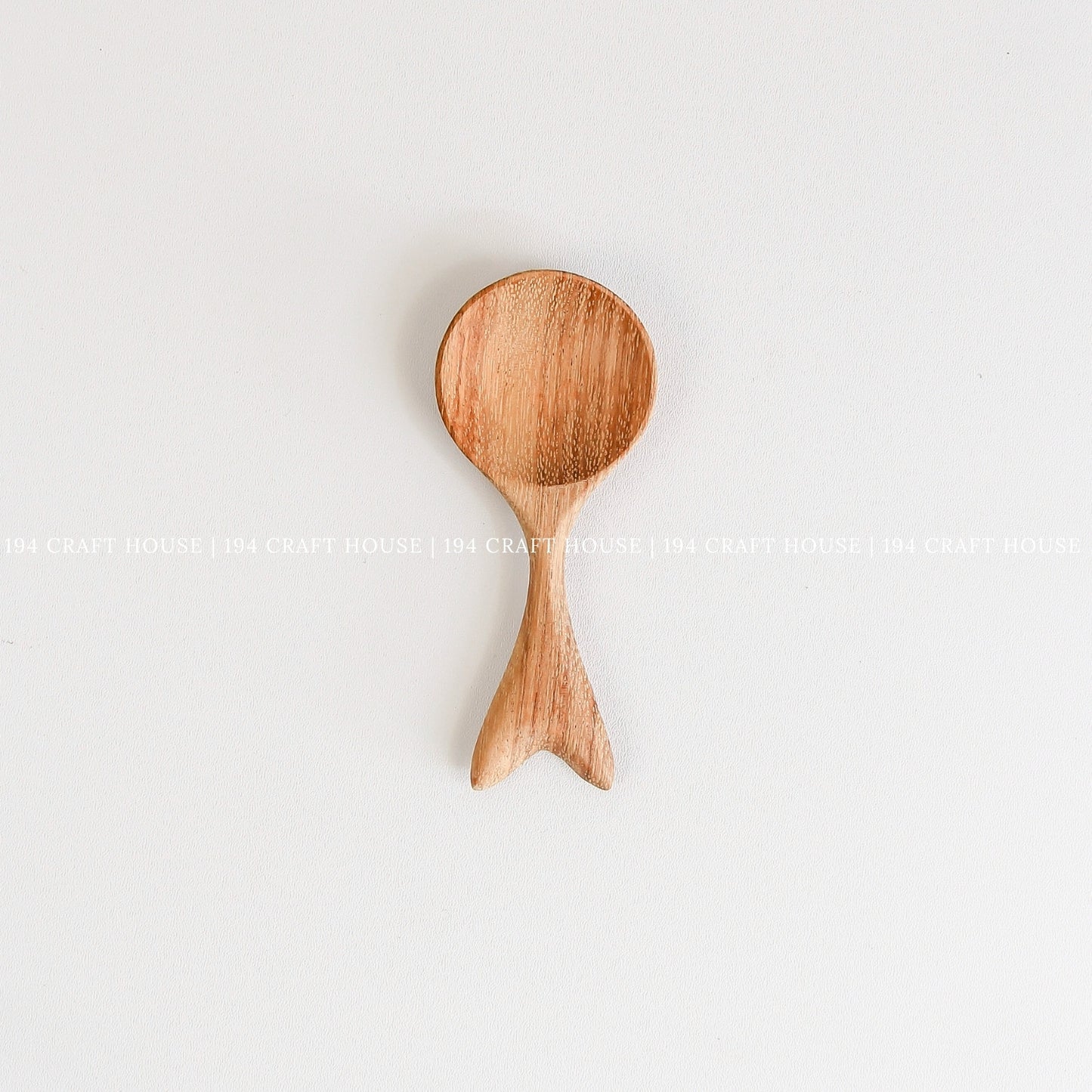 Handcrafted small wooden spoon with a decorative fishtail-shaped handle and smooth natural wood grain